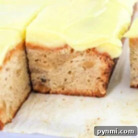 A slice of Banana and Nuts Cake, beautifully frosted, sits on a white surface, revealing the delightful crunch of visible nuts.