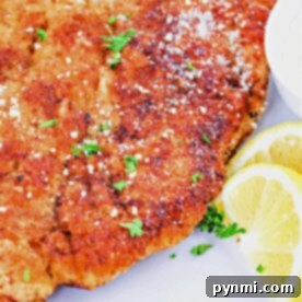 A close-up of breaded baked chicken cutlets whose perfect timing is essential, garnished with fresh herbs and served alongside zesty lemon slices on a pristine white plate.