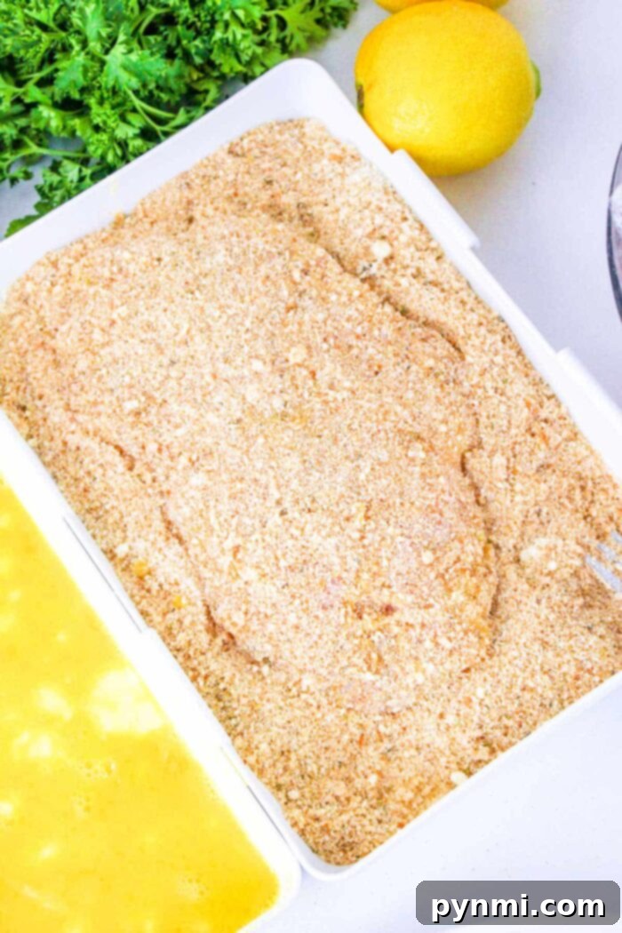 The Best Baking Time for Chicken Cutlets 7 Breaded chicken breast cutlet on a tray, ready to answer the question of how long to bake chicken cutlets, with egg wash and parsley nearby.