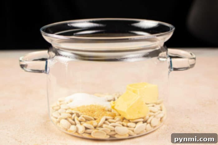 A glass pot with butter beans, butter, sugar, and spices inside rests on a light surface. Its reminiscent of preparing a comforting dish like butter beans—simple yet satisfying in its blend of ingredients.