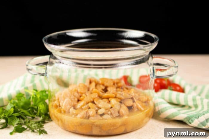 A glass pot filled with butter beans sits beside fresh parsley and cherry tomatoes on a striped cloth, offering inspiration on how to cook butter beans with a touch of garden-fresh simplicity.