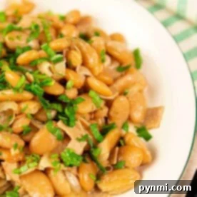 A plate of cooked butter beans garnished with fresh parsley captures your attention, while cherry tomatoes and a striped cloth create the perfect backdrop. Discover how to cook butter beans to achieve this deliciously vibrant dish.