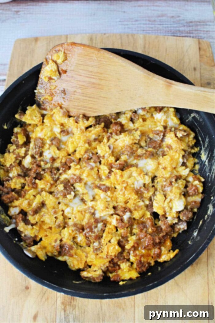 A frying pan on a wooden cutting board contains scrambled eggs mixed with ground sausage. A wooden spatula rests on the edge of the pan, partially covered in the egg and sausage mixture—a perfect demonstration of how to cook chorizo and eggs.