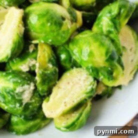 A close-up of boiled Brussels sprouts seasoned with herbs and crumbled cheese on a white plate.