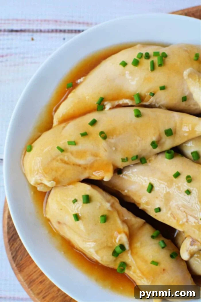Perfectly boiled chicken tenders served on a pristine white plate, drizzled with soy sauce and garnished with fresh green onions, showcasing their tender and succulent texture achieved by precise boiling.