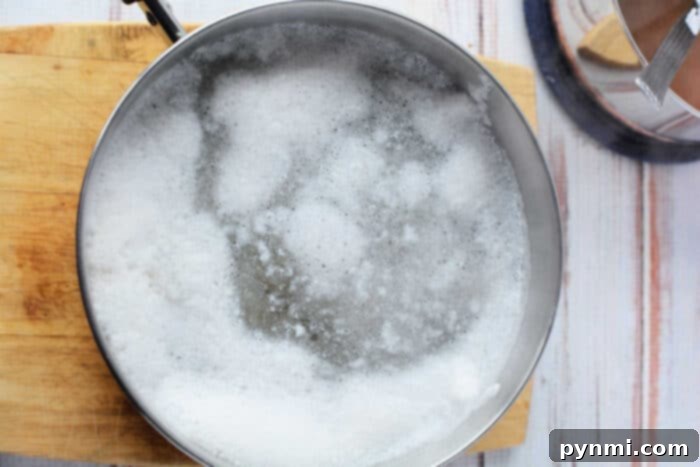 Two hands carefully lifting cooked chicken tenders from a pot of boiling water using a wire skimmer, illustrating the final step in how to boil chicken to perfection.
