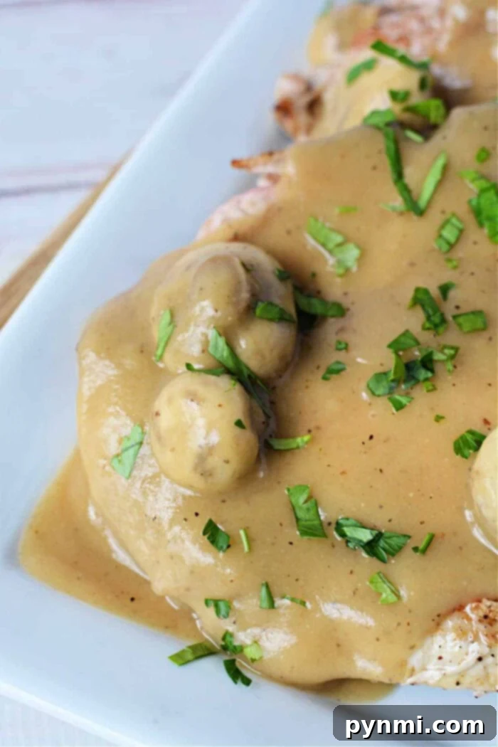 Skillet Pork Chops with Savory Mushroom Gravy 7 Plated pork chop with creamy mushroom gravy, garnished with fresh parsley.