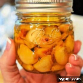 A hand tenderly holds a jar of preserved garlic cloves in oil, capturing the essence of how to make garlic confit.