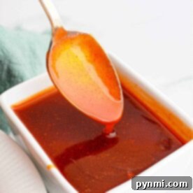 A silver spoon drizzling vibrant red Popeyes Sweet Heat Sauce into a pristine white square dish.