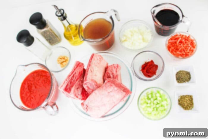 A collection of ingredients for a recipe arranged on a white surface, including raw beef short ribs perfect for Short Rib Tacos, tomato sauce, beef broth, diced onions, shredded carrots, chopped celery, red wine, tomato paste, minced garlic, cooking oil, salt, pepper and dried herbs.