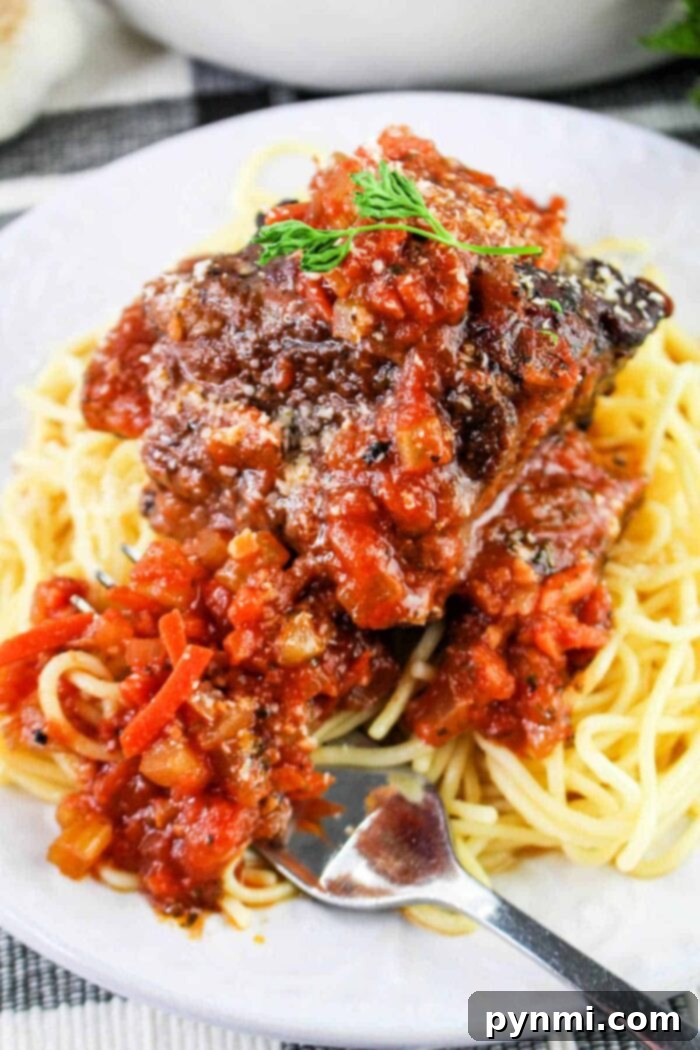 A plate of spaghetti topped with a hearty portion of meat sauce garnished with herbs sits invitingly on a checkered cloth. A fork rests on the edge, ready for use, reminiscent of the anticipation before savoring delicious short rib tacos.