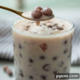 A glass of creamy bubble tea showcases a spoon lifting perfectly cooked tapioca pearls, set against a soft focus background. Learn how to cook boba for bubble tea and achieve this delightful texture at home.