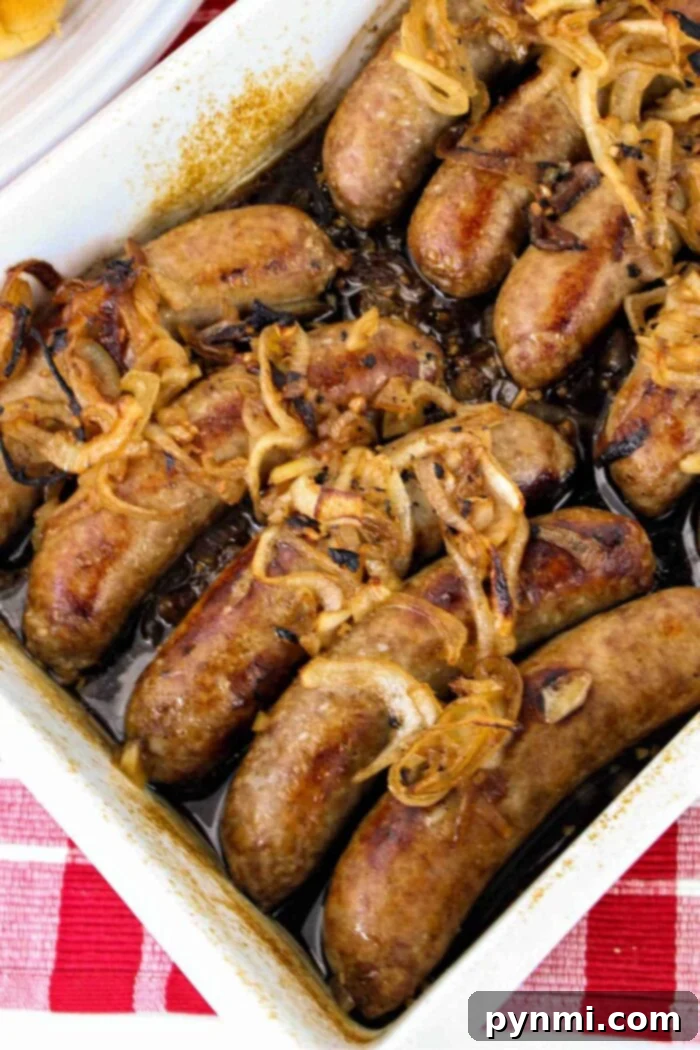 Unlocking Bratwurst Perfection 2 A rectangular baking dish filled with perfectly cooked bratwurst sausages, topped with sweet caramelized onions, rests on a festive red and white checkered tablecloth. The image captures the inviting essence of a classic German meal, showcasing bratwurst cooked to perfection.