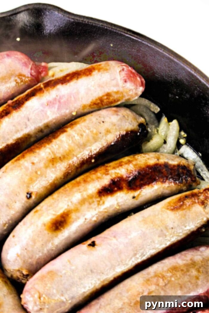 Unlocking Bratwurst Perfection 6 Five sausages are expertly cooking in a robust cast iron skillet, showcasing a beautifully browned, crispy exterior. They are nestled on a flavorful bed of sliced onions, creating an enticing aroma. The overhead perspective of the pan offers a delectable hint on how to cook bratwurst to perfect crispness and tenderness.