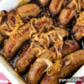 A rectangular baking dish filled with cooked sausages topped with caramelized onions sits enticingly on a red and white checkered tablecloth, making you wonder how to cook bratwurst to perfection.