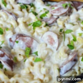Creamy macaroni with sliced kielbasa and parsley in a skillet, stirred with a wooden spoon—a delightful pasta recipe thats both hearty and satisfying.