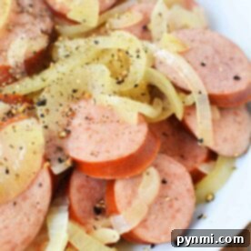 Sliced sausage and onions seasoned with black pepper on a white plate, reminiscent of a simple recipe for Kielbasa in Crock Pot.