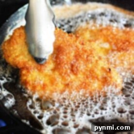 Crispy Chicken Cutlets 8 Tongs holding a golden-brown fried chicken cutlet sizzling in hot oil.