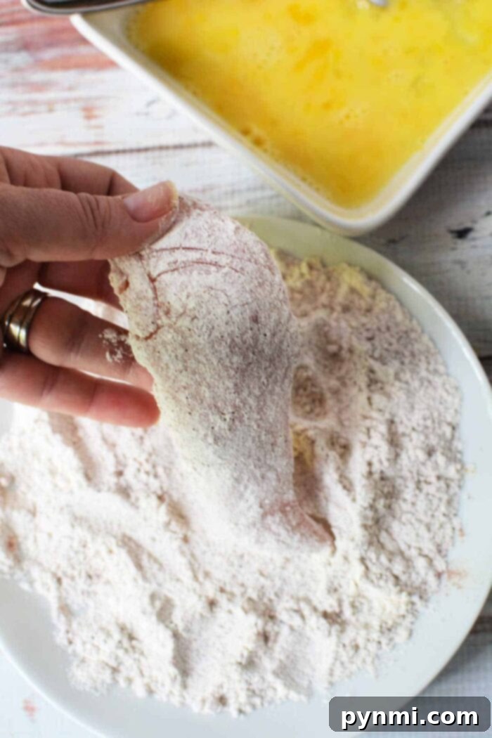 Hand dipping chicken fillet in flour, with beaten eggs nearby, this process mirrors the initial steps of learning how to make chicken tenders.