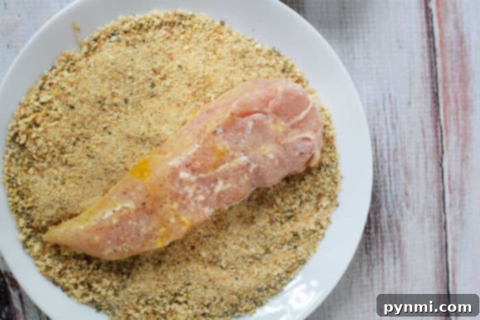 Learn how to make chicken tenders by breading raw chicken breast on a white plate, achieving that perfect crispy texture.