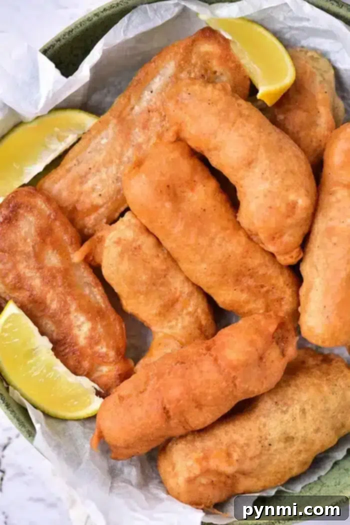 Secrets to Great Beer Batter 2 A plate of golden-brown beer-battered fish pieces is arranged on parchment paper in a bowl. Two lemon wedges are placed alongside the fish, adding a zesty contrast to the savory delight.