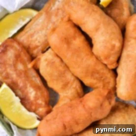 A basket of golden-brown, beer-battered fish pieces accompanied by lemon wedges rests delicately on parchment paper.