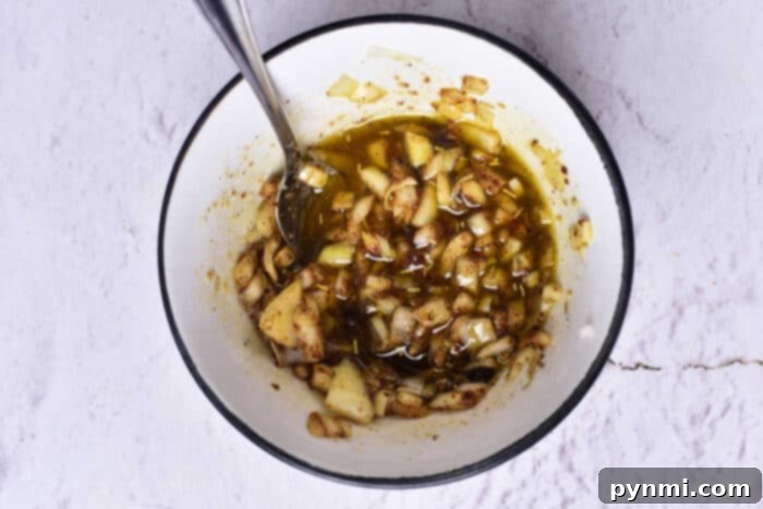 Rich confit oil infused with whole garlic cloves and fresh herbs, ready to envelop pork for a slow, flavorful cooking process.