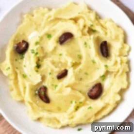 A bowl of garlic confit mashed potatoes topped with roasted garlic cloves and sprinkled with fresh parsley.