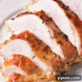 Mastering Turkey Breast Confit 7 A close-up of several slices of cooked turkey breast confit on a white plate. The turkey has a crispy, browned skin with herbs visible on the surface. The inside appears tender and juicy.