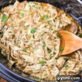 Crockpot Green Chili Chicken simmers gently as shredded chicken blends with herbs.