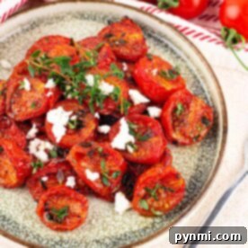A plate of roasted cherry tomatoes, prepared in a Ninja Foodi, is elegantly garnished with fresh herbs and crumbled feta cheese.