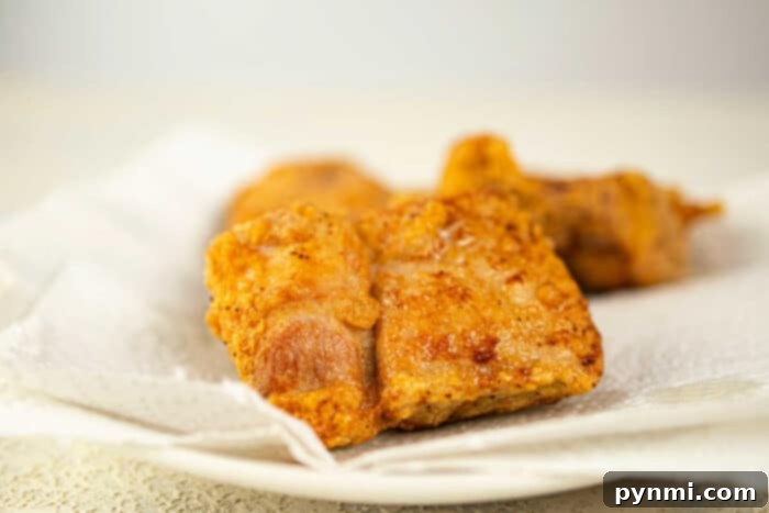 Ultimate Crispy Pork Chops 6 Close-up of crispy fried pork pieces, reminiscent of deep-fried pork chops, resting on a paper towel-lined plate.