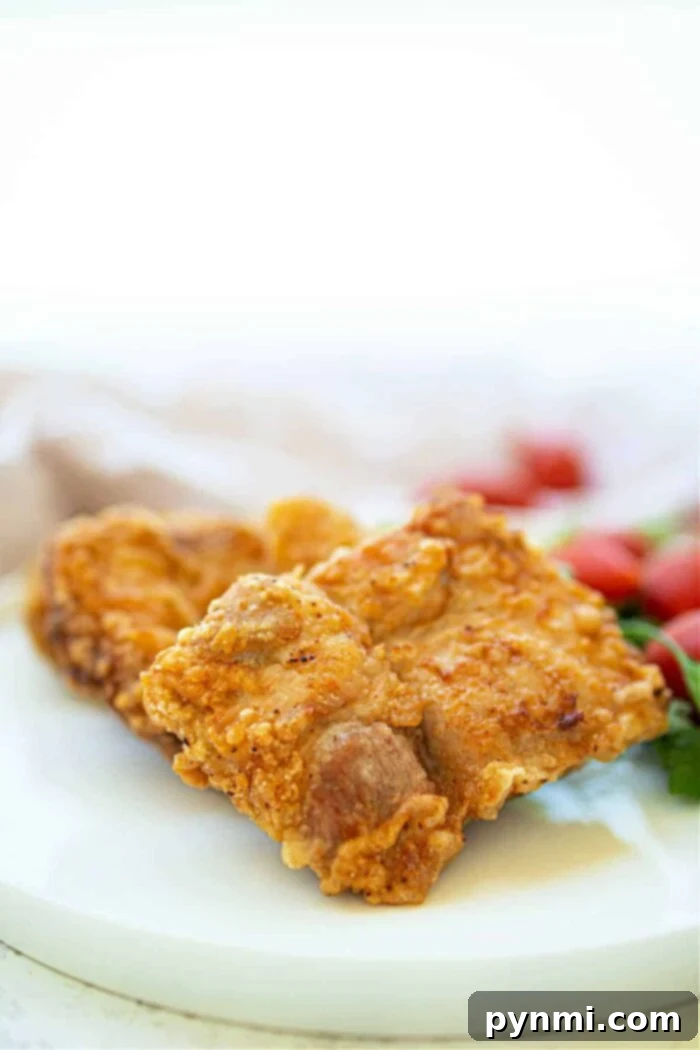 Ultimate Crispy Pork Chops 7 Crispy fried pork pieces share the plate with deep-fried pork chops, while cherry tomatoes brighten the background.