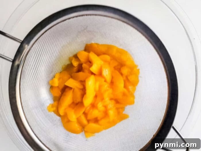 Drained canned peaches ready for the dessert filling, showcasing their vibrant color and readiness for mashing.