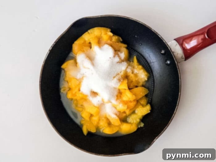 Chopped peaches with sugar in a frying pan, cooking down to create a sweet and luscious filling for peach bars.