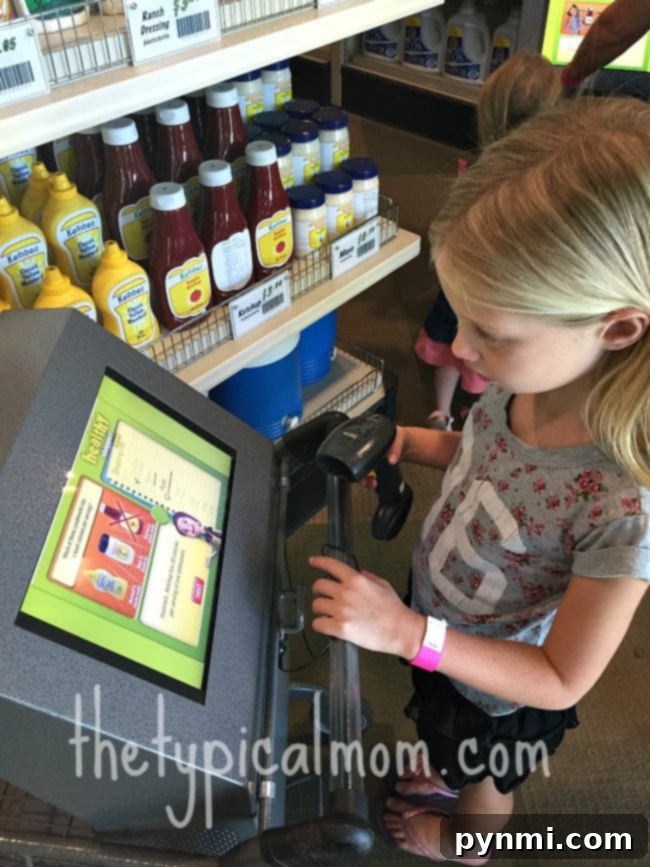 The interactive grocery store exhibit at Discovery Cube OC, Santa Ana, where children learn about nutrition and consumer skills through play. In a detailed miniature grocery aisle filled with condiments, a girl intently uses a touchscreen kiosk. This immersive setup, reminiscent of an interactive exhibit at the Discovery Science Center Santa Ana, merges digital learning with a playful, real-world shopping adventure.