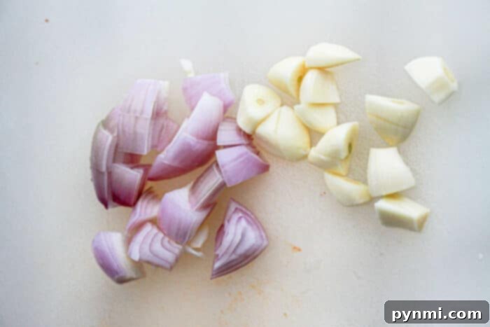 Fiery Garlic Chili Paste 3 Chopped pieces of red onions and garlic cloves are arranged on a white cutting board, showcasing key aromatic components for a homemade Garlic Chili Paste Recipe.