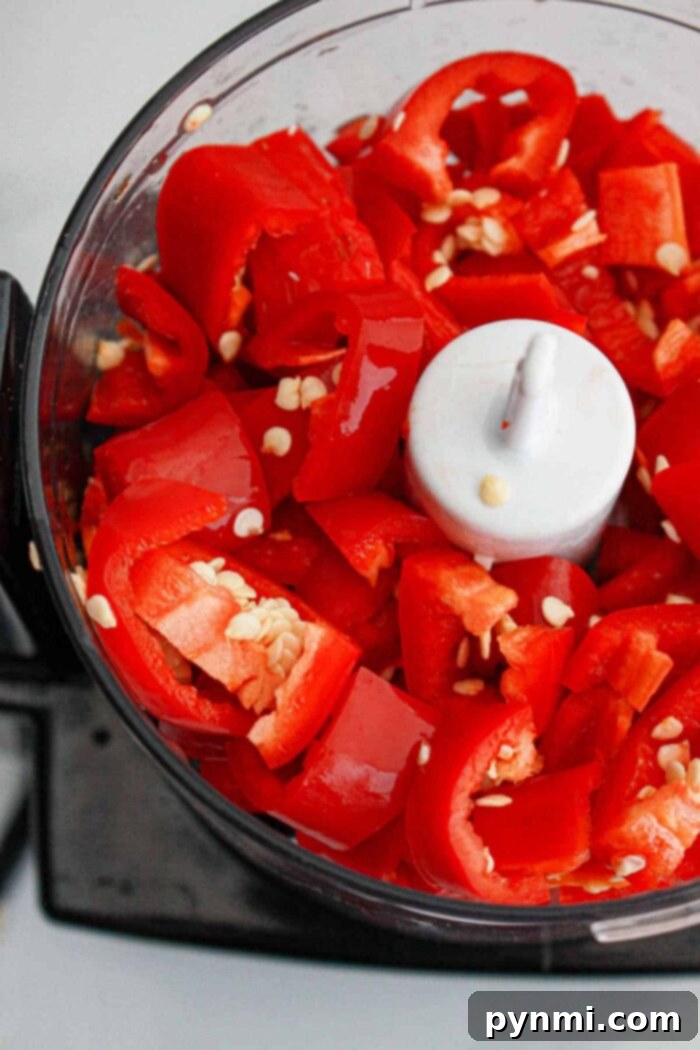 Fiery Garlic Chili Paste 5 A food processor bowl filled with coarsely cut red bell peppers, some visible seeds, and hints of garlic, ready for blending into a flavorful homemade chili paste.