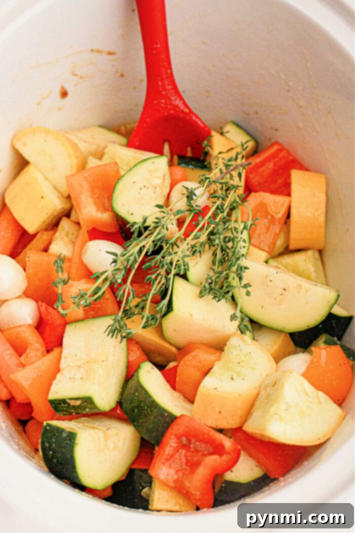 A red spoon rests in a pot filled with chopped fresh vegetables, including zucchini, bell peppers, and onions. A sprig of thyme is placed on top, adding a touch of green to the mix. The seasoned vegetables appear ready for cooking in a slow cooker.