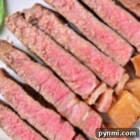 A plate with several slices of medium-rare beef strip loin steaks arranged in a line. The meat is pink in the center with a browned outer edge, featuring a juicy texture. Some greens are visible in the corner of the plate.