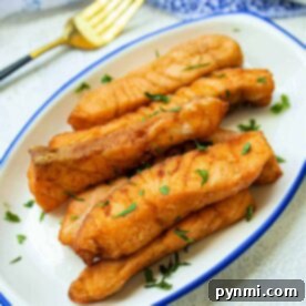 A plate of golden brown deep-fried salmon fillets garnished with parsley, with a fork and ketchup in the background.