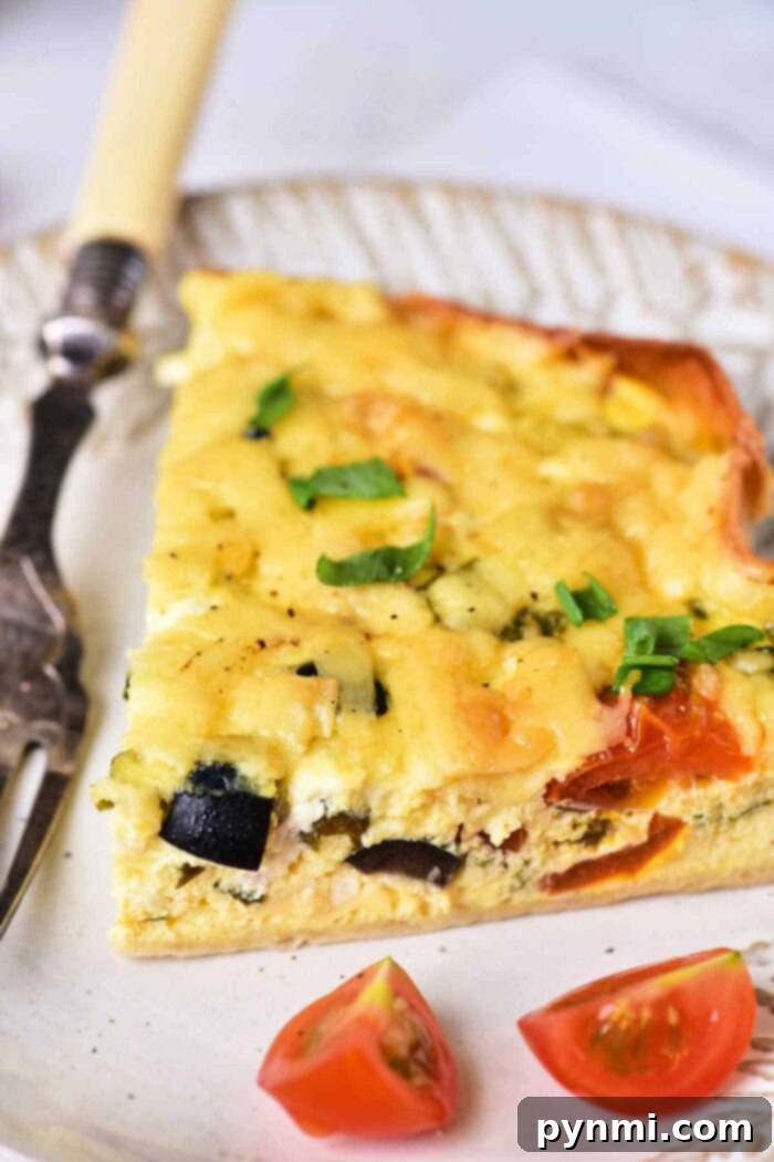 Light and Creamy Cottage Cheese Quiche 7 A perfectly cooked slice of vegetable cottage cheese quiche rests on a white plate. The quiche reveals distinct pieces of zucchini and tomato within its creamy filling, crowned with a generous layer of melted cheese and a sprinkle of fresh chopped green onions. A decorative fork is placed alongside, and two bright cherry tomato halves garnish the plate.