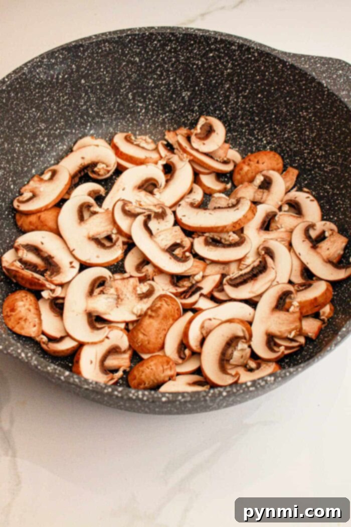 Set-It-and-Forget-It Biscuits and Gravy 4 Raw sliced mushrooms filling a black speckled frying pan, ready for cooking on a light-colored countertop to prepare the hearty Slow Cooker Biscuits and Gravy breakfast.