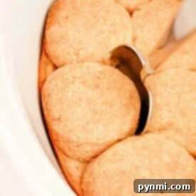 Slow Cooker Biscuits and Gravy. There is a silver spoon resting on top of one of the golden brown biscuits. The biscuits are arranged close together in the dish.