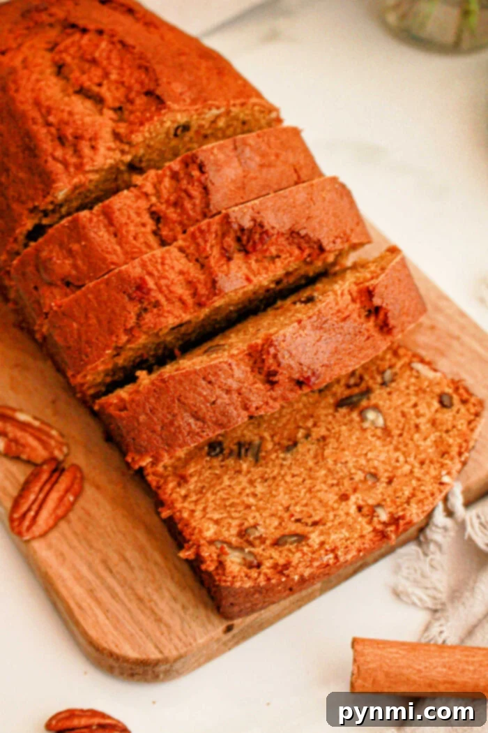 A sliced loaf of banana nut bread sits on a wooden cutting board, with some pecan halves scattered around. The bread has a golden-brown crust and visible pecan pieces in each slice, reminiscent of Sweet Potato Bread with Cake Mix. A small piece of cloth and a cinnamon stick are partially visible beside the board.