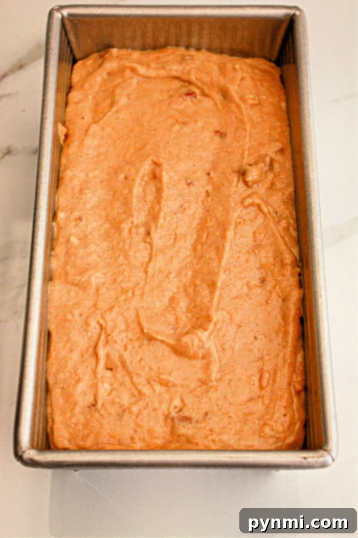 A metal loaf pan filled with unbaked sweet potato bread batter made with cake mix sits on a white surface. The batter appears smooth and evenly spread within the pan, ready for baking.