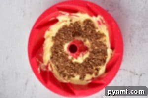 Bundt pan with cake batter, using the classic Sock it to me cake recipe with cake mix, topped with a crumble layer and placed on a textured light surface.