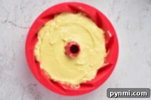 A red bundt pan filled with yellow cake batter sits invitingly on a light gray surface, ready to transform into a delightful Sock it to me cake using a convenient cake mix.
