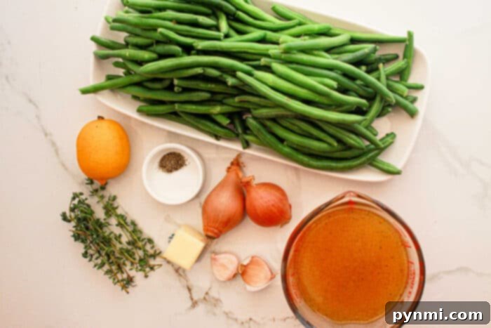 Tender Slow Cooker Green Beans 4 A display of ingredients on a white marble surface: a rectangular dish filled with fresh green beans, perfect for the crockpot, a whole lemon, small glass bowls with black pepper and broth, two shallots, a pat of butter, two garlic cloves, and a few sprigs of thyme.