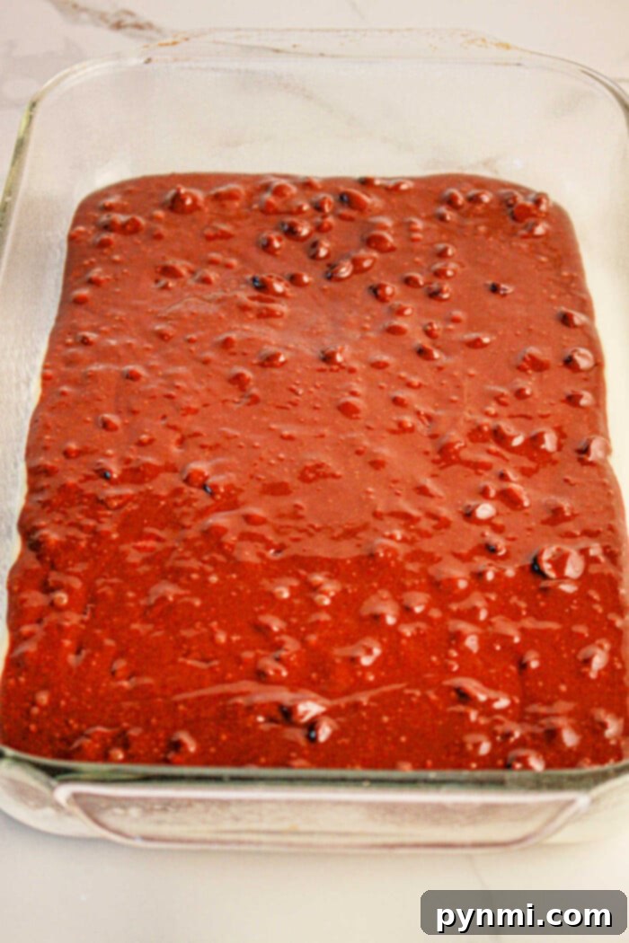 Ultimate Brownie Cookie Dough Brookie Bars 3 A clear glass baking dish filled with thick, dark chocolate brownie batter, smooth and ready for the next layer. This image perfectly illustrates the initial step of creating brookies by combining a rich brownie base with cookie dough, all set on a light-colored countertop.